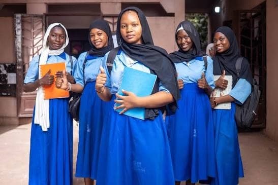 Groupe d'élèves souriantes, cahiers à la main, dans la cour de l'école